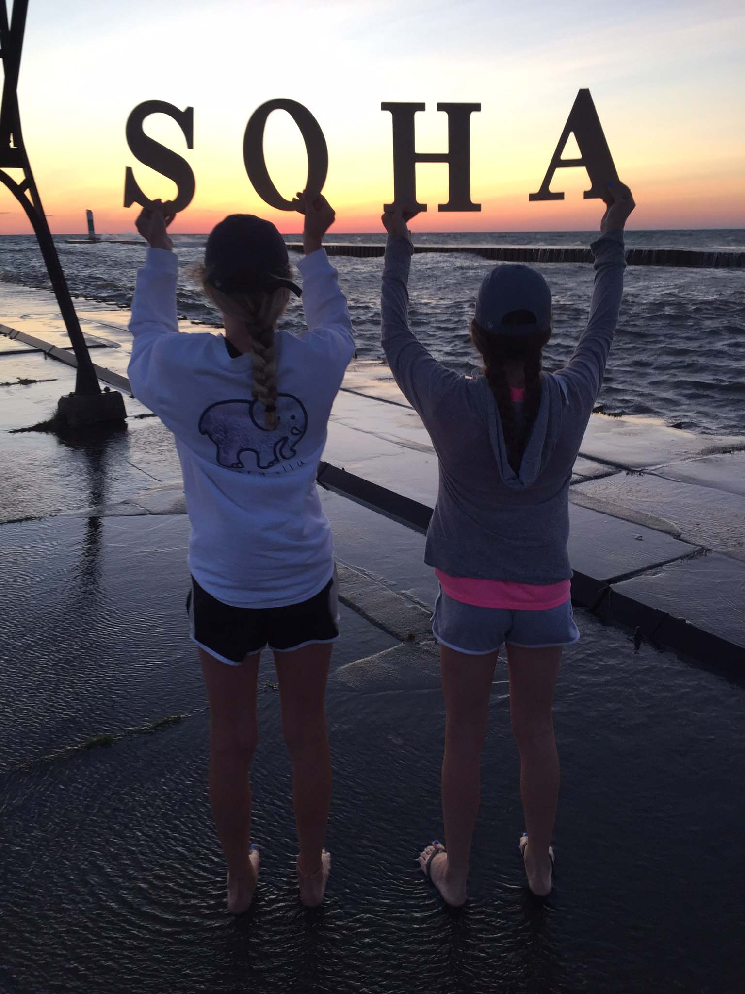 Two girls holding sign with the sunset in background