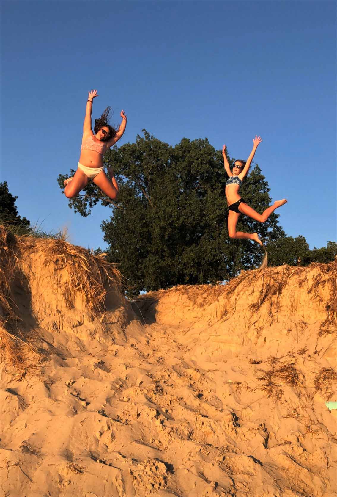 Two girls jumping off a sand cliff with excitement