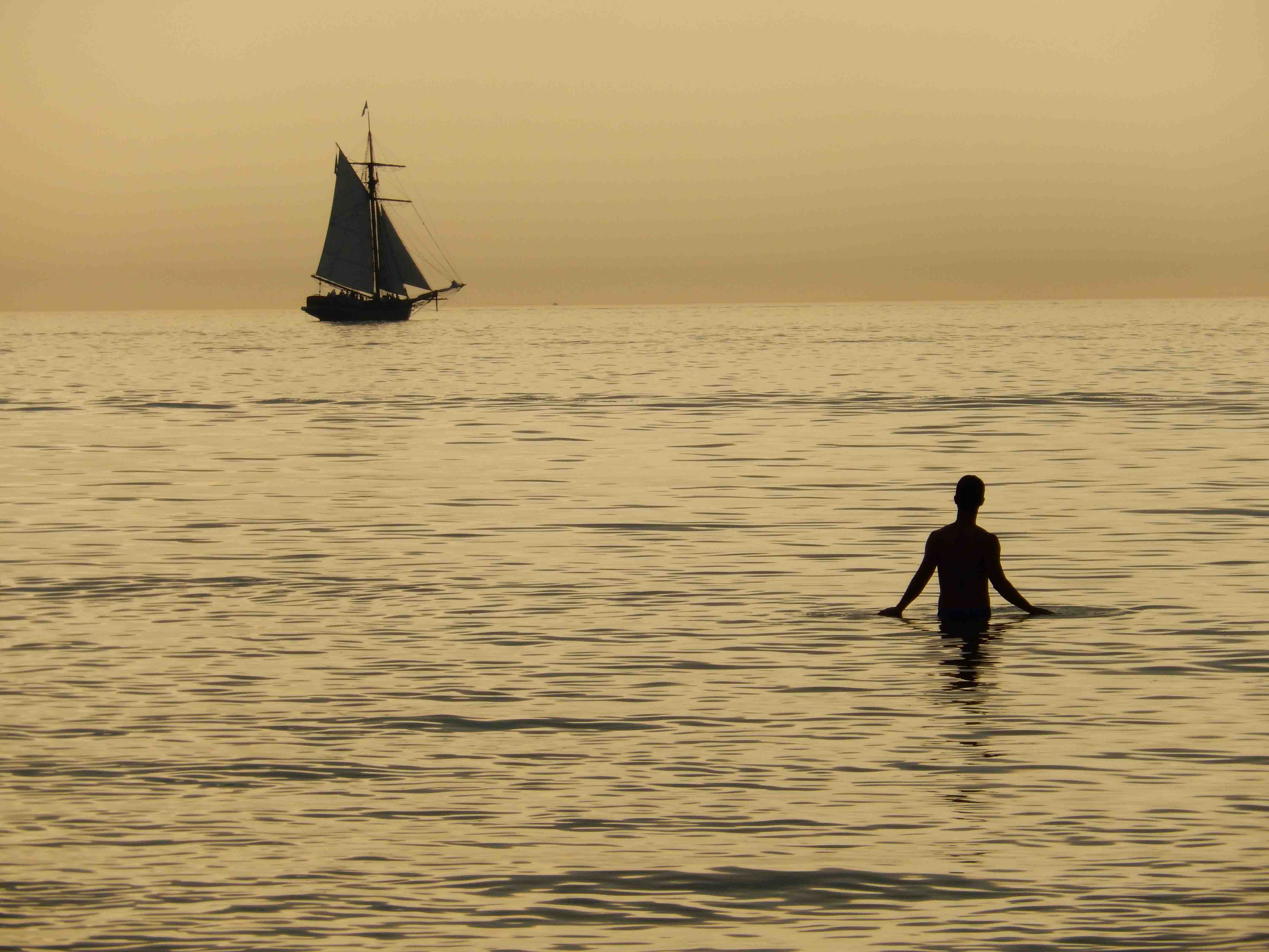 Photo of a man in the water with a boat in the distance