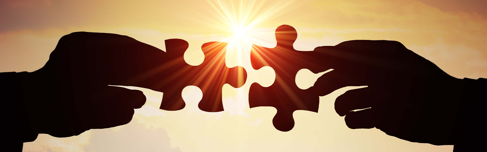 Two people holder connecting puzzle pieces in the sunset