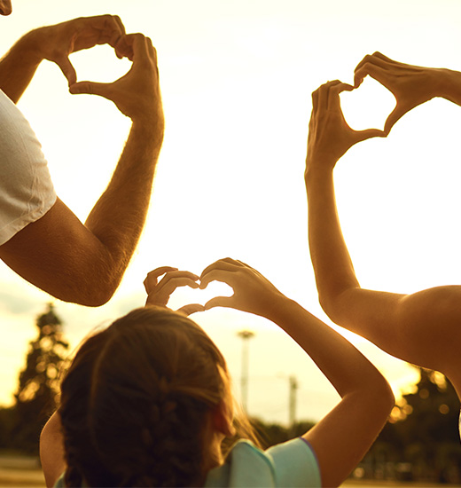 family holding their hands in a heart shape with sunset in the background
